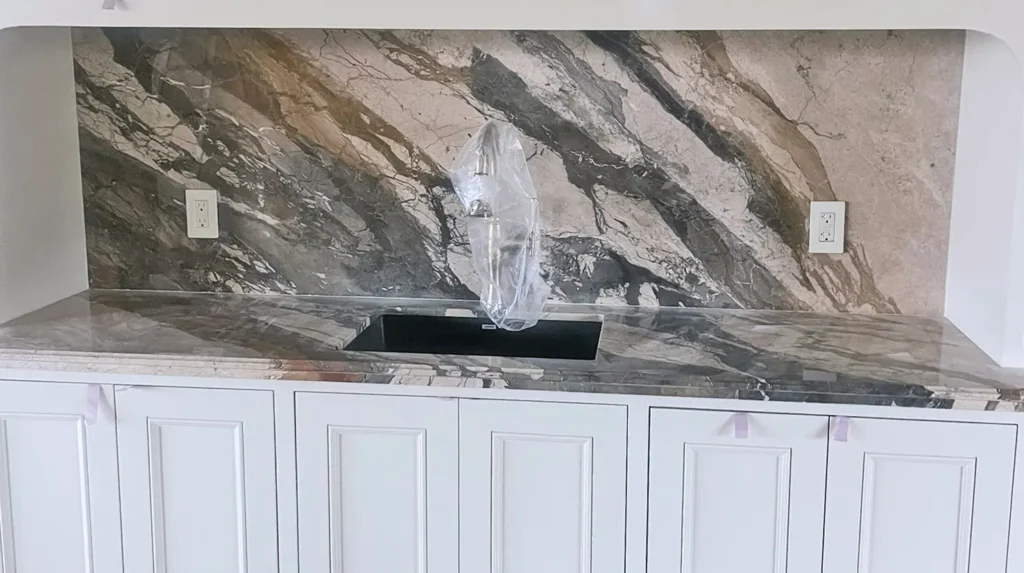Breccia Fantastica marble countertop and full-height backsplash installed in a custom kitchen featuring dramatic blue-gray, cream, and gold veining.