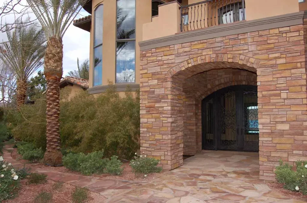 Luxury home entrance clad in Tupelo Honey meta quartzite with natural stone veneer walls, arched entry, and matching exterior paving.