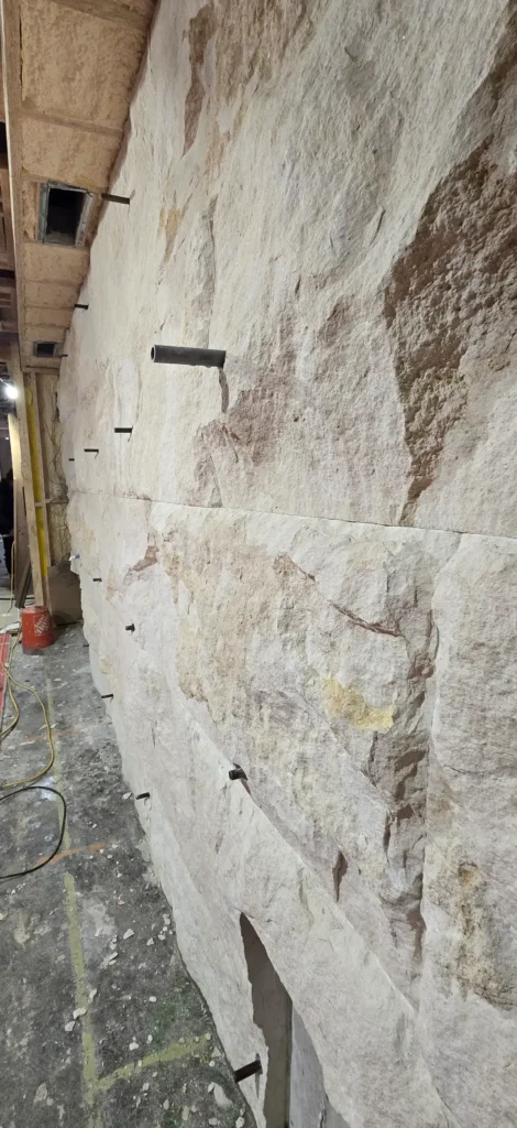 Custom natural stone rock wall by The World of Stone featuring large irregular stone panels and integrated architectural penetrations