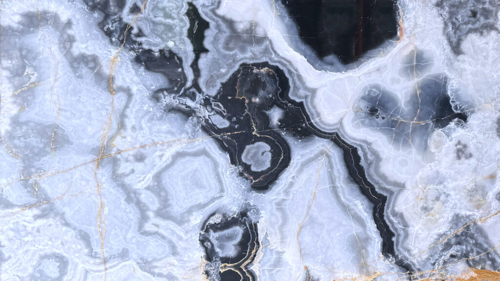 Close-up of Silver Grey Onyx slab showing concentric charcoal-black formations, translucent silver-gray crystalline banding, and delicate gold veining.